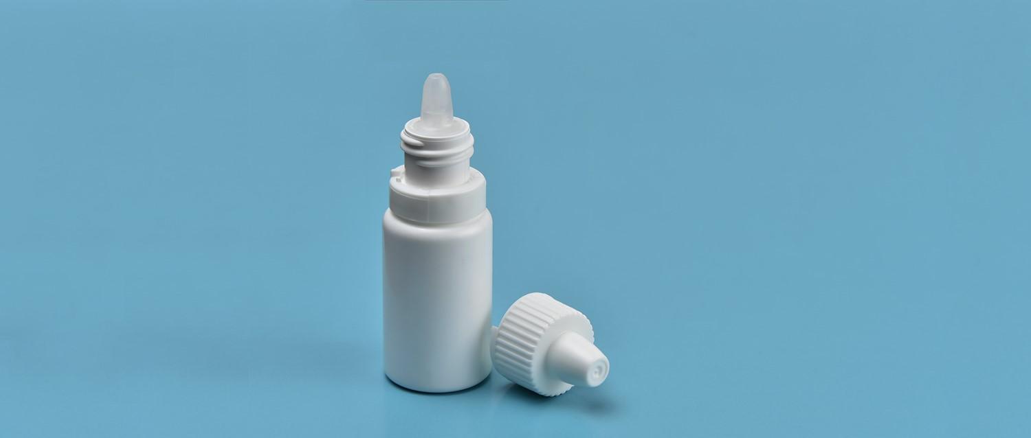 White eye drop or nasal spray bottle with its cap removed, displayed against a light blue background.