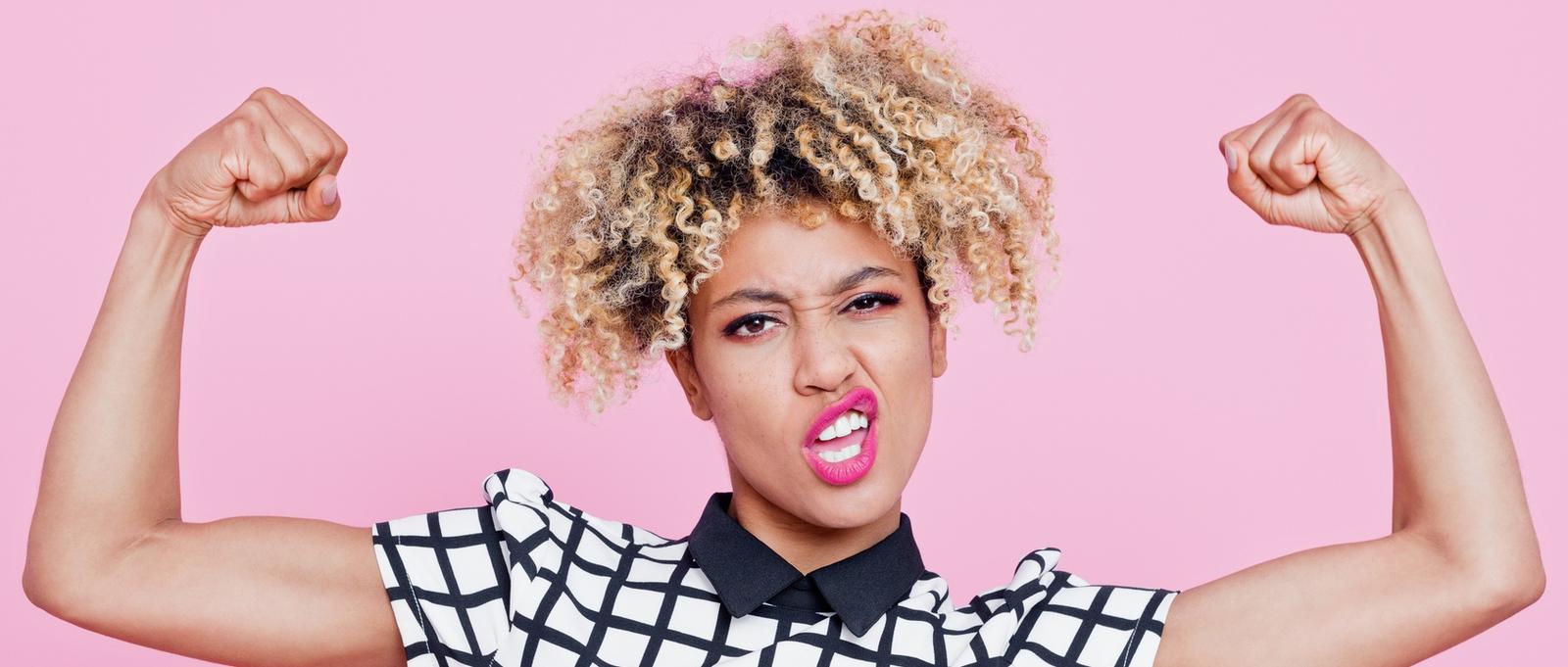 Studio portrait of strong afro American young woman flexing muscles.