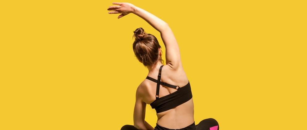 Back view athlete woman with hair bun in tight top and pants sitting in lotus position on gym mat practicing yoga, bending to side with raised hand, doing stretching workouts. studio shot isolated.
